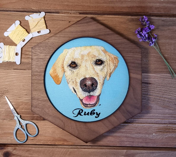 Hand embroidered portrait of golden Labrador called Ruby on light blue fabric in a hexagonal frame