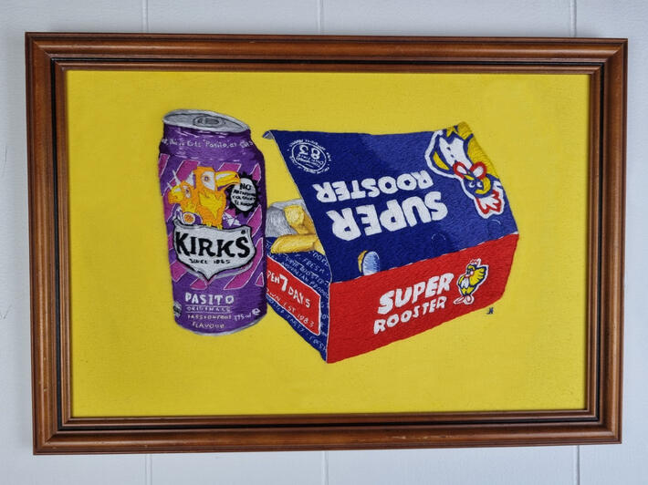 Hand embroidery of a can of Pasito and a box of Super Rooster hot chips on a bright yellow fabric background.