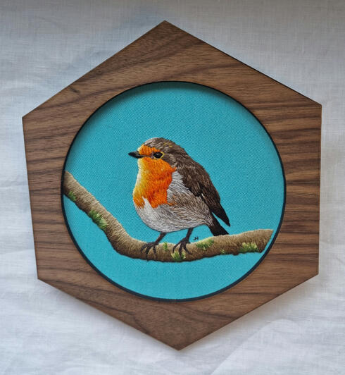 Hand embroidered portrait of an English Robin on light blue fabric in a hexagonal frame