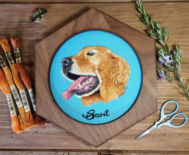 Hand embroidered portrait of golden retriever called Basil on light blue fabric in a hexagonal frame