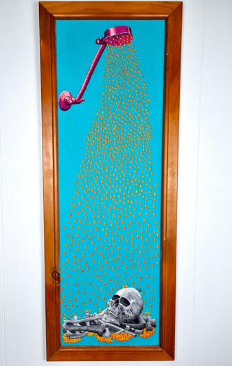 A long and narrow frame with teal fabric houses a hand embroidery depicting a bright pink and purple shower head raining down bright orange and yellow water onto a greyscale pile of bones and a skull, sitting in a puddle of orange and yellow water.