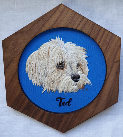 Hand embroidered portrait of a white fluffy dog called Ted on dark blue fabric in a hexagonal frame